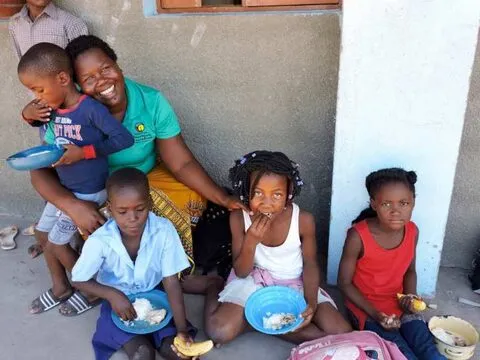 Uma mulher sorridente com crianças pequenas a almoçar no degrau de uma escola