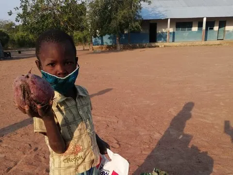 Um rapaz de máscara mostra uma beterraba do cabaz de alimentos da família