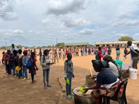 Uma longa fila de almoço num pátio escolar em direção às panelas