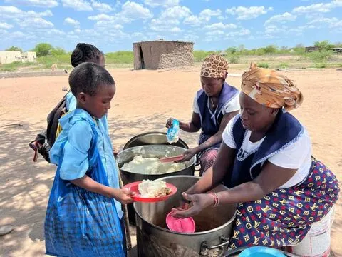 Uma cozinheira serve uma menina de uma panela grande