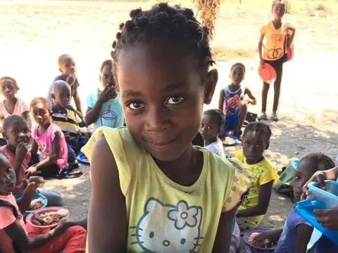 Uma menina de blusa amarela segura o prato do almoço entre outras crianças