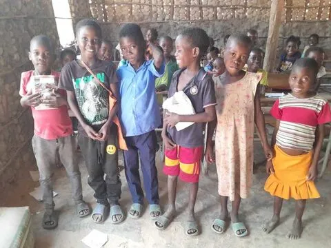 Alunos de pé juntos numa sala de aula de paredes de barro