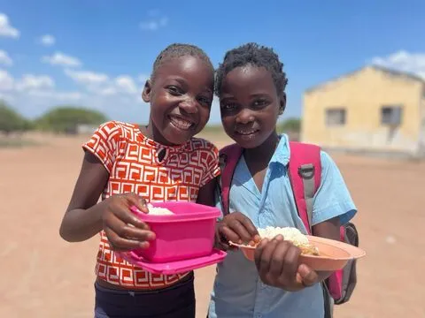 Duas meninas sorridentes mostram o seu almoço escolar de arroz e caril