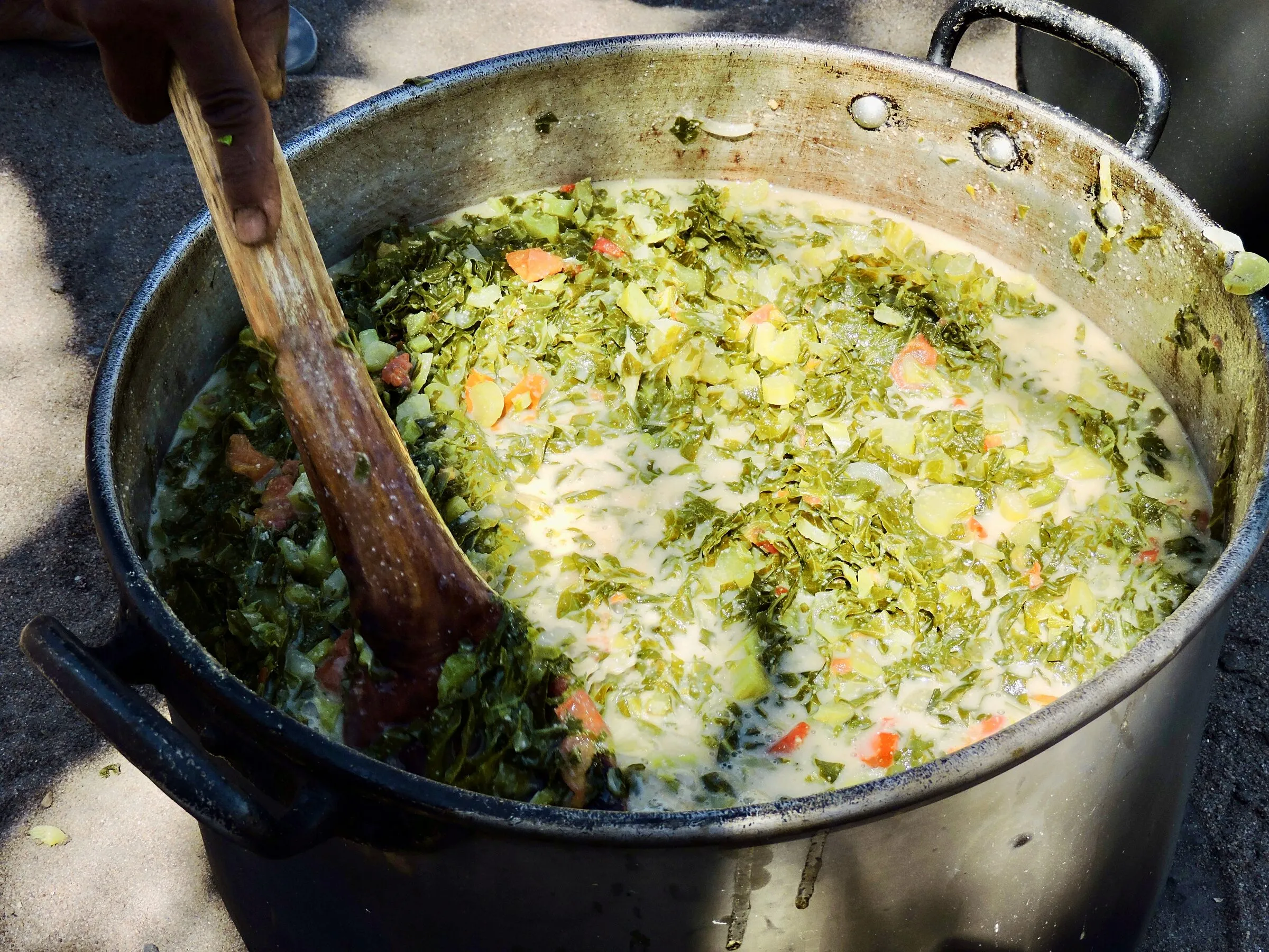 Uma panela grande de caril de couve com amendoim, mexida com uma pá de madeira