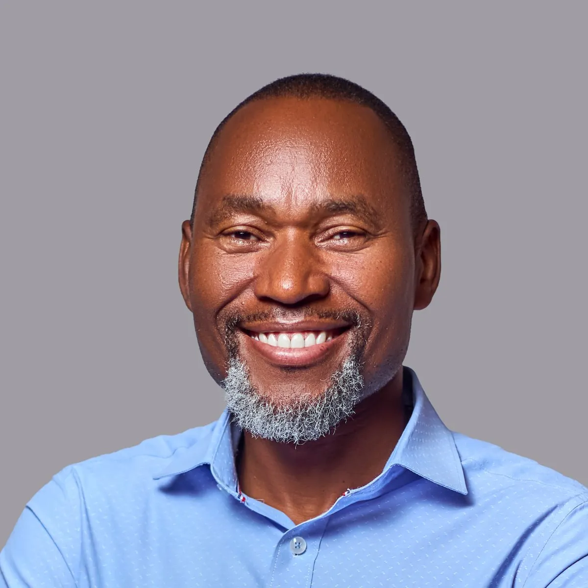 Roberto Mutisse com um largo sorriso, barba grisalha e camisa azul-clara